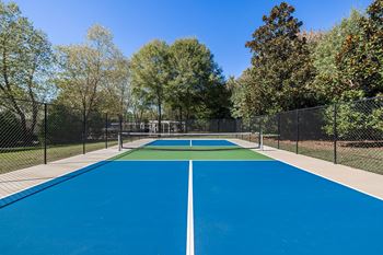 A blue tennis court surrounded by a fence and trees.